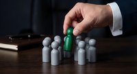 Business hand selecting green figure from gray crowd representing leadership recruitment talent acquisition and human resources management in corporate environment.