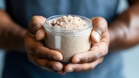 Hands holding glass jar with homemade chocolate protein powder supplement, nutritious superfood blend with cocoa dust on top, healthy fitness nutrition.