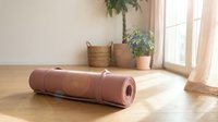 Pink yoga mat rolled on wooden floor in bright living room with plants and natural light for home fitness workout and meditation practice.