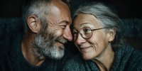 Happy senior couple embracing and smiling together showing love and affection in intimate moment. Elderly man with gray beard and woman with glasses.
