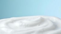 Soft white cream swirl texture on light blue background for skincare cosmetics and beauty product advertising campaigns.