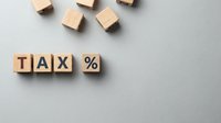 Wooden blocks spelling tax percent symbol on gray surface with scattered cubes for accounting, finance, and business tax planning concepts.