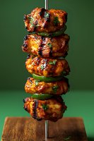 Grilled chicken kebab with green peppers stacked on metal skewer, glazed with spicy marinade showing char marks and garnished with fresh herbs on wooden surface.