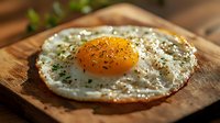 Sunny side up fried egg with herbs and spices on rustic wooden cutting board, macro food photography with soft natural lighting and shallow depth of field.