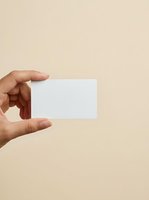 Hand holding blank white business card against neutral beige background, ideal for branding, corporate identity, and mockup design projects.