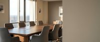 Modern conference room with wooden table and leather chairs overlooking city skyline through large windows for corporate meetings and business presentations.