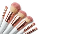 Cosmetic brushes with white handles and rose gold ferrules arranged in a row against white background for makeup application and beauty product promotion.