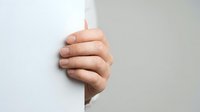 Close-up of a hand peeking around a white corner wall, showing thumbs up gesture for approval, success, and positive feedback in business and communication contexts.