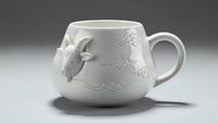White ceramic mug with decorative pig figurine and ornate floral patterns for kitchen decor and beverage serving.