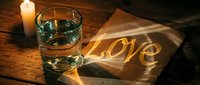 Romantic candlelit scene with a glass of water and the word Love glowing on a wooden table, evoking warmth, intimacy, and heartfelt emotion.