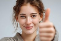 Young Caucasian woman with natural freckles showing thumbs up gesture against light gray background, expressing positivity and approval.