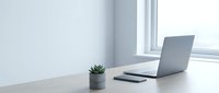Minimalist workspace with open laptop, smartphone, and small potted succulent plant on white desk by bright window for remote work and productivity.