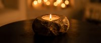 Rustic stone candle holder with flickering flame creates warm ambient lighting on dark wooden surface in cozy interior setting for relaxation and meditation.