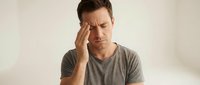 Middle-aged Caucasian man experiencing headache or stress, holding head with hand while sitting. Health and wellness concept for medical presentations.