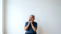 Senior man with gray hair and beard, Caucasian ethnicity, wearing navy blue t-shirt, hands on face expressing joy and amazement against white background, isolated for design use.