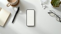 Smartphone with blank screen surrounded by office supplies, eyeglasses, coffee cup, succulent plant and notebook on white desk for app mockup and digital marketing.