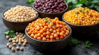 Variety of colorful legumes and pulses in rustic ceramic bowls with fresh herbs. Raw organic chickpeas, red kidney beans and yellow lentils on dark background.