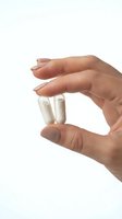 Hand holding two white capsules between fingers on isolated white background for healthcare and pharmaceutical design concepts.