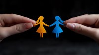 Hands holding paper cut figures of two women in orange and blue, symbolizing unity, friendship and support against dark background. For social campaigns.