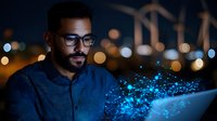 Young African American businessman in glasses working on laptop at night with glowing blue digital particles effect, modern technology concept for business solutions.