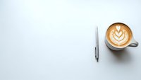 Minimalist workspace with latte art coffee cup and pen on clean white desk surface for business and productivity concepts.