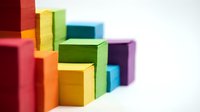 Stacked colorful wooden blocks in red, yellow, green, blue, and purple arranged in abstract formation on white background for design projects.