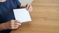Man in dark blue shirt holding blank white card on wooden table surface for mockup or presentation purposes.