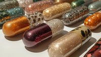 Colorful pharmaceutical capsules with glittery metallic finishes arranged on white surface for medical and healthcare design projects.