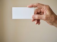 Male hand holding blank white business card against neutral beige background, suitable for branding, corporate identity, and marketing mockup designs.