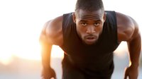 Athletic African American man doing push-ups during golden hour workout outdoors. Fitness training exercise routine for strength building and muscle development.