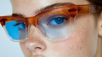 Close up view of bright blue eye with freckles seen through stylish brown gradient transparent eyeglasses frame against light background, beauty and fashion concept.