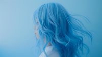 Young Asian woman with flowing blue dyed hair against light blue background, profile view showing ethereal movement and soft dreamy aesthetic for beauty and fashion concepts.