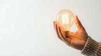 Hand holding glowing light bulb against white background symbolizing creativity innovation and bright ideas for business concepts.
