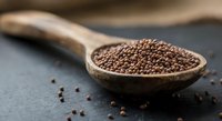 Coriander seeds in wooden spoon on dark slate surface. Aromatic spice ingredient for cooking, seasoning and culinary preparations in kitchen.