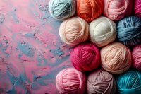 Colorful yarn balls in pastel and bright tones arranged on abstract pink and blue painted background, perfect for crafting and knitting projects, creative hobby concept.