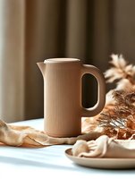 Modern beige ribbed ceramic pitcher on white table with soft natural lighting and dried flowers, creating minimalist aesthetic composition for home decor styling.