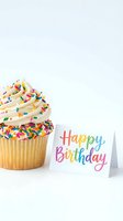 Vanilla cupcake with colorful sprinkles and swirled frosting next to a rainbow Happy Birthday card on white background.