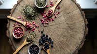 Wooden spoons filled with colorful dried herbs, spices and berries arranged on rustic tree stump cross-section for natural cooking and wellness concepts.