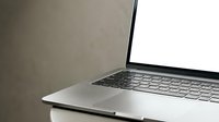 Modern silver laptop computer with blank white screen open on neutral beige surface, minimalist workspace setup for business presentations and mockups.