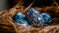 Traditional blue Easter eggs with white floral folk art pattern nestled in natural straw nest, selective focus on detailed ornamental design and rustic setting.
