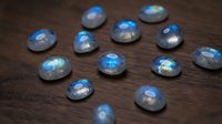 Collection of polished labradorite gemstones with blue flash scattered on dark wooden surface for jewelry making and crystal healing practices.