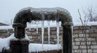 Frozen water pipe with icicles hanging from metal fitting during winter freeze, plumbing maintenance and cold weather protection concept.