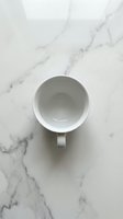 Empty white ceramic mug on marble surface, overhead view. Minimalist kitchen styling for beverage, coffee, tea, and tableware design projects.