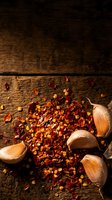 Chopped red chili peppers and onion halves scattered on rustic wooden surface with warm golden lighting, suitable for culinary, cooking, recipe, and food preparation projects.