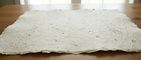 Handmade white paper sheet with natural deckled edges and visible fiber texture on wooden surface for crafting and artistic projects.