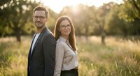 Happy young professional couple with glasses standing together in golden sunset light outdoors in nature park for lifestyle photography.