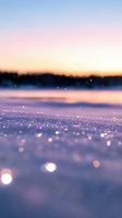 Sparkling snow crystals glowing at sunset with dreamy bokeh effect and pink sky reflection creating magical winter atmosphere on frozen lake surface.