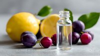 Essential oil bottle with fresh lemon and plums on light background, natural aromatherapy ingredients for skincare and wellness.