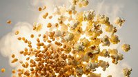 Flying popcorn kernels scattered in air with golden lighting creating dynamic motion effect for snack food advertising and entertainment concepts.