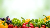 Fresh organic vegetables and herbs border on soft green background with copy space for healthy eating and nutrition concepts.